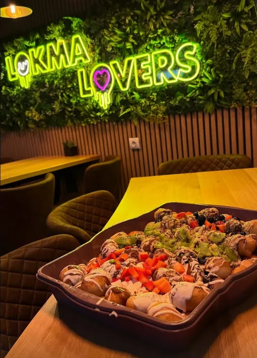 Leuchtschrift „Lokma Lovers“ vor grüner Pflanzenwand im Lokal